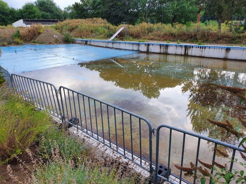 Das Bild zeigt ein marodes Schwimmbecken im Außenbereich.
