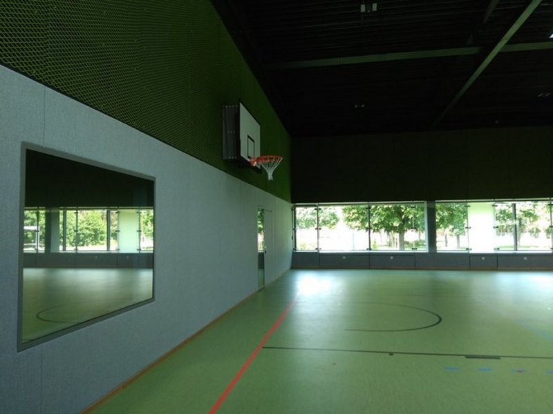 Das Bild zeigt eine Sporthalle mit grünem Boden und einer Fensterfront im Hintergrund.