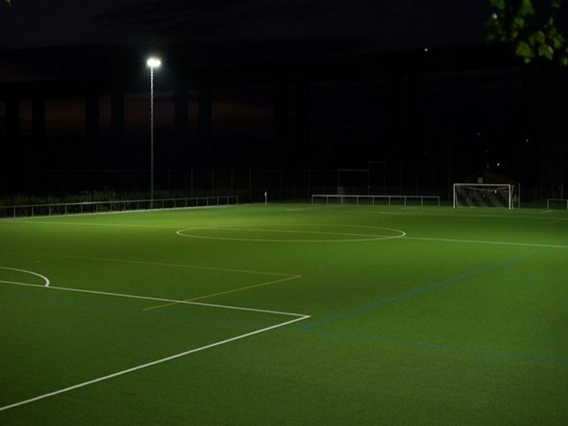 Das Bild zeigt einen Fußballplatz bei Nacht mit Flutlichtbeleuchtung.