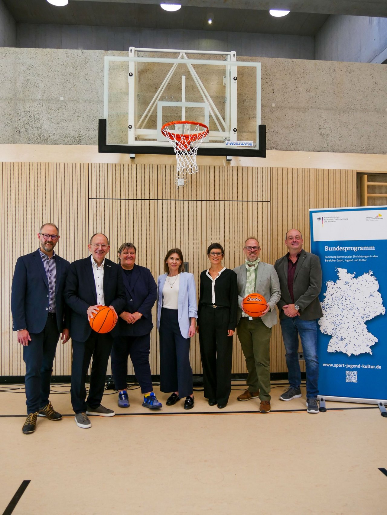 Quelle: Benan Benjamin Schroeder für Stadt Mannheim Das Bild zeigt mehrere Personen unter einem Basketballkorb in einer Sporthalle, zwei von ihnen halten einen Basketball in Händen.