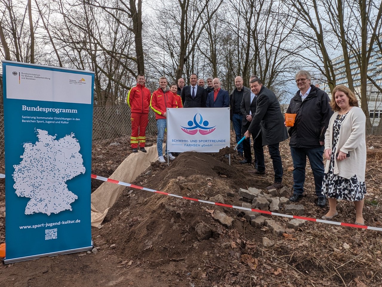 Quelle: Bezirksamt Wandsbek Auf dem Bild sind eine Gruppe Menschen auf dem Baugelände zu sehen, einer von ihnen schaufelt symbolisch für den etwas Erde.