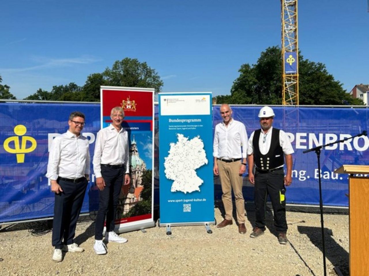 Quelle: Stadt Hannover Das Bild zeigt vier Personen vor zwei Roll-Ups auf einer Baustelle. Das Roll-Up zeigt zeigt das Bundesprogramm Sport, Jugend und Kultur.