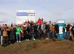 Das Bild zeigt eine große Gruppe von Menschen auf einer Baustelle. Die Personen im Vordergrund halten Schaufeln. Einzelne Personen jubeln.