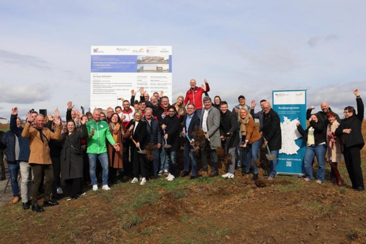 Quelle: Gemeinde Wölfersheim Das Bild zeigt eine große Gruppe von Menschen auf einer Baustelle. Die Personen im Vordergrund halten Schaufeln. Einzelne Personen jubeln.