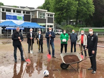 Das Bild zeigt mehrere Personen mit Spaten auf matschigem Untergrund, ein Mann im Bildvordergrund fährt einen Schubkarren.