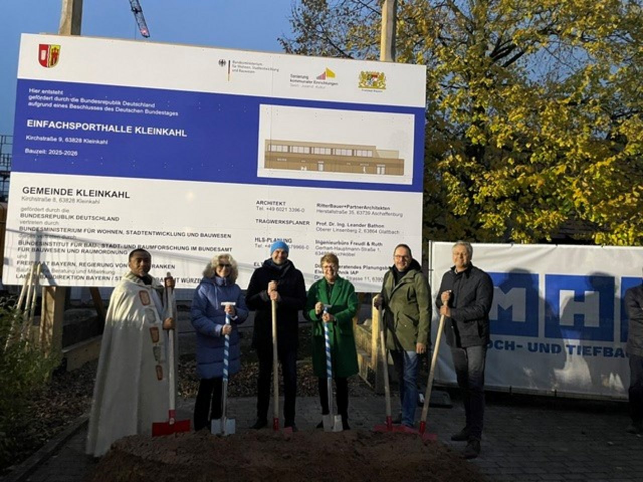 Quelle: Gemeinde Kleinkahl Man sieht sechs Personen mit Spaten die vor einem Bauschild zur Einfachsporthalle Kleinkahl stehen.