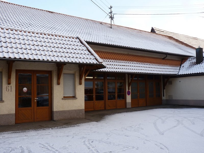 Man sieht eine Sporthalle im Winter mit verschneitem Dach und Vorhof.