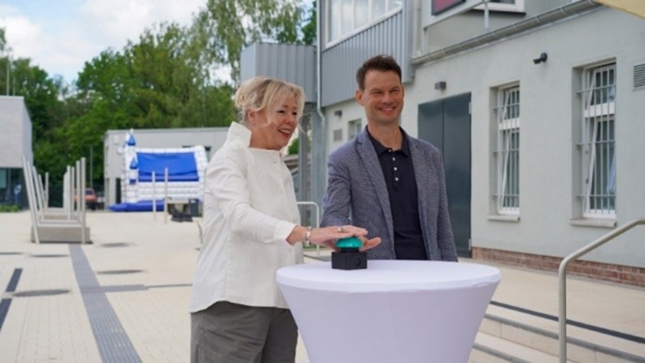 Das Bild zeigt zwei Personen die gemeinsam auf einen Buzzer auf einem Tisch drücken.