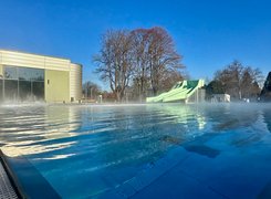 Quelle: Bäder, Sport und Freizeit Salzgitter GmbH Das Bild zeigt ein Außenschwimmbecken mit einer Rutsche und einem Gebäude im Hintergrund