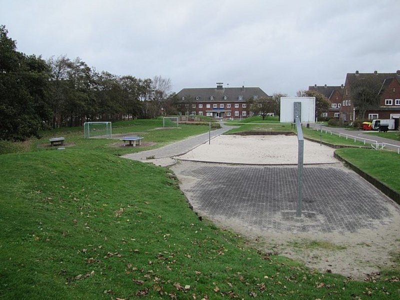 Das Bild zeigt verschiedene Sportanlagen auf einer Wiese, einen Sandbereich und einen Basketballkorb.