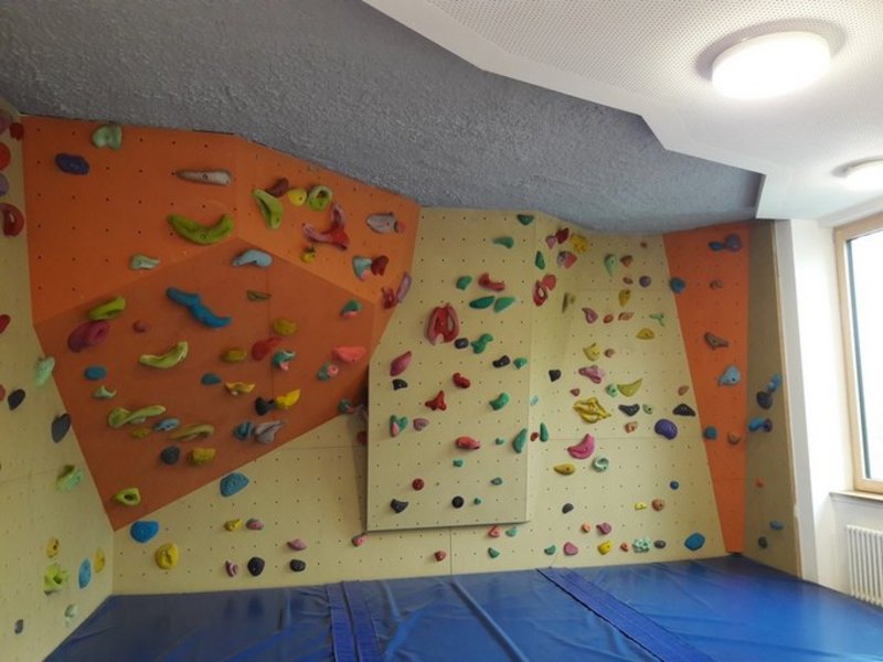 Das Bild zeigt eine bunte Indoor-Kletterwand mit blauem Mattenboden darunter.