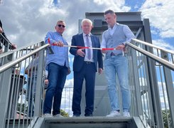 Das Bild zeigt drei Männer auf der oberen Schwelle einer Außentreppe, einer von ihnen schneidet ein Band durch.