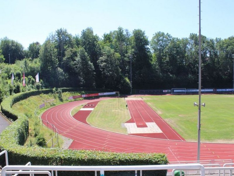 Das Bild zeigt eine Sportplatzanlage mit Rasenfläche und roter Rundbahn sowie weiteren Spielflächen.