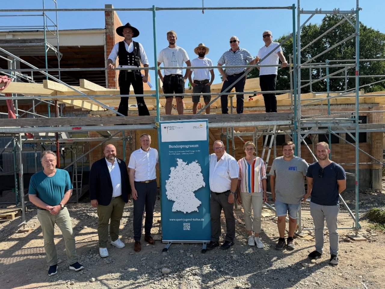 Ein Bild von mehreren Menschen, die vor oder auf einem Baugerüst auf einer Baustelle stehen. 