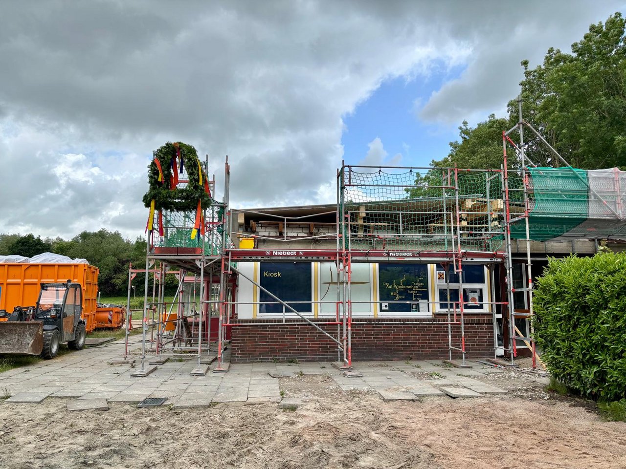 Das Bild zeigt ein eingerüstetes Bungalow-Gebäude mit Richtkranz am Dach.