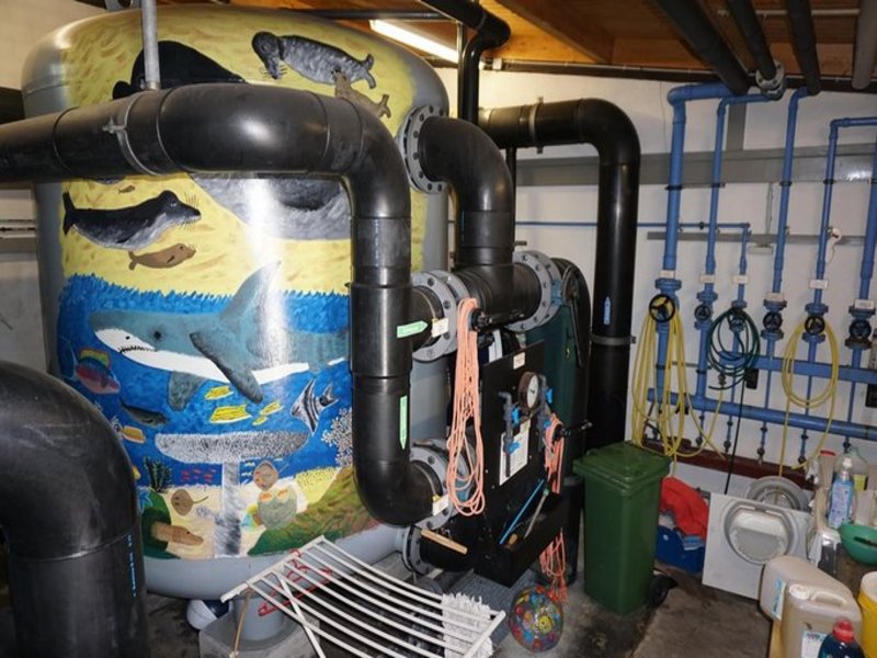 Das Bild zeigt eine Technikanlage mit Rohren und einem Tank, der mit Tieren aus der Meereswelt bemalt ist.