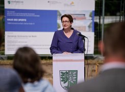 Quelle: Henning Schacht Man sieht eine Frau, die an einem Rednerpult vor einem Bauschild steht und eine Rede hält.