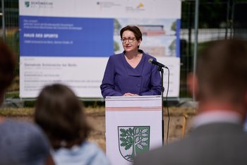 Quelle: Henning Schacht Man sieht eine Frau, die an einem Rednerpult vor einem Bauschild steht und eine Rede hält.
