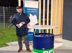 Quelle: PSV Wismar / Jana Hennig Man sieht einen Mann vor einem Stehtisch und einem Roll-Up zum Bundesprogramm, der eine Rede hält.