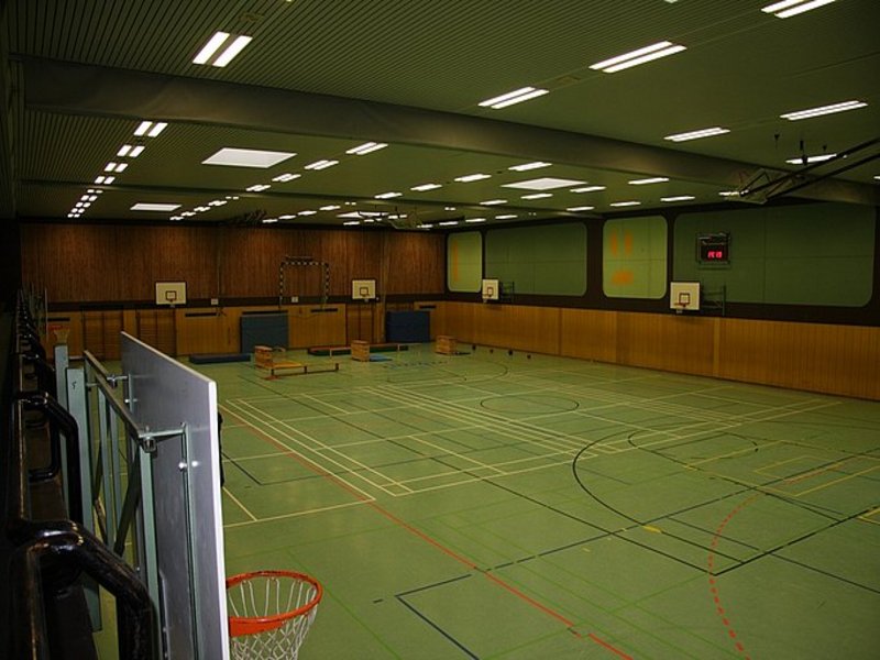 Das Bild zeigt eine Sporthalle mit verschiedenen Sportgeräten und düster wirkender Beleuchtung.