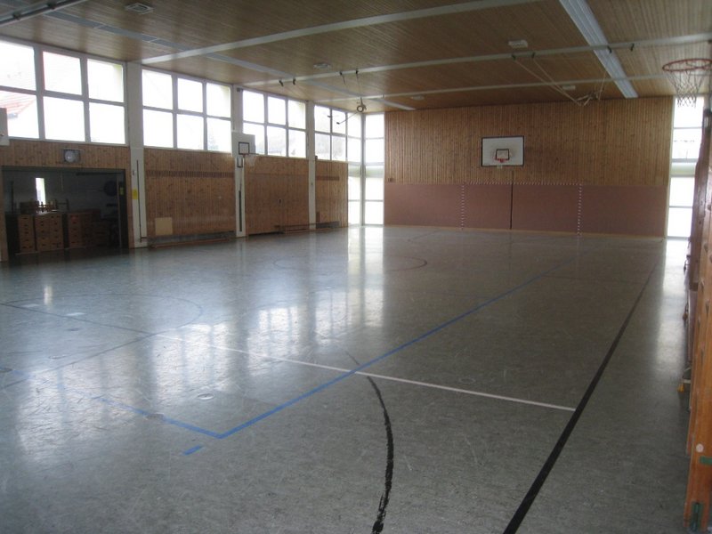 Man sieht eine große Halle mit Sportboden und Linien für verschiedene Spielarten.