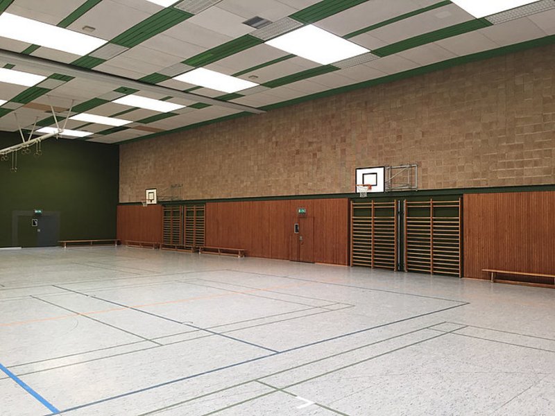 Das Bild zeigt eine Sporthalle mit hellem Boden und holzverkleidenten Wänden.