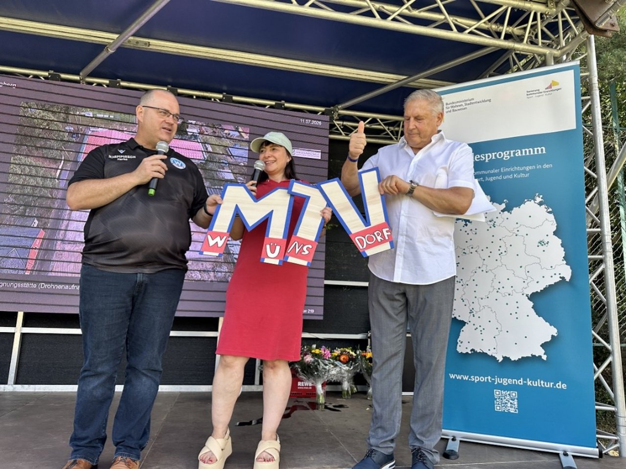 Quelle: Stadt Zossen Das Bild zeigt drei Personen auf einer Bühne. Die Personen halten die Buchstaben "M" und "T" und "V" in den Händen.