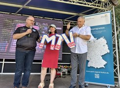 Quelle: Stadt Zossen Das Bild zeigt drei Personen auf einer Bühne. Die Personen halten die Buchstaben "M" und "T" und "V" in den Händen.