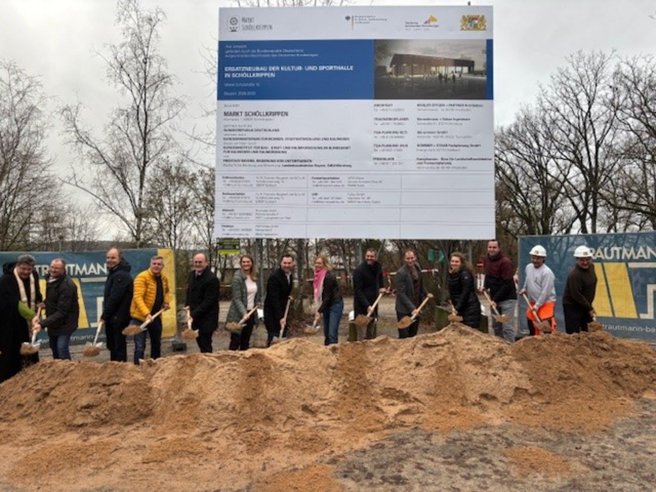 Quelle: Markt Schöllkrippen Das Bild zeigt einen Spatenstich. Eine Gruppe von Menschen mit Baustellenhelmen und Spaten sticht in einen Erdhaufen vor einem Bauschild.
