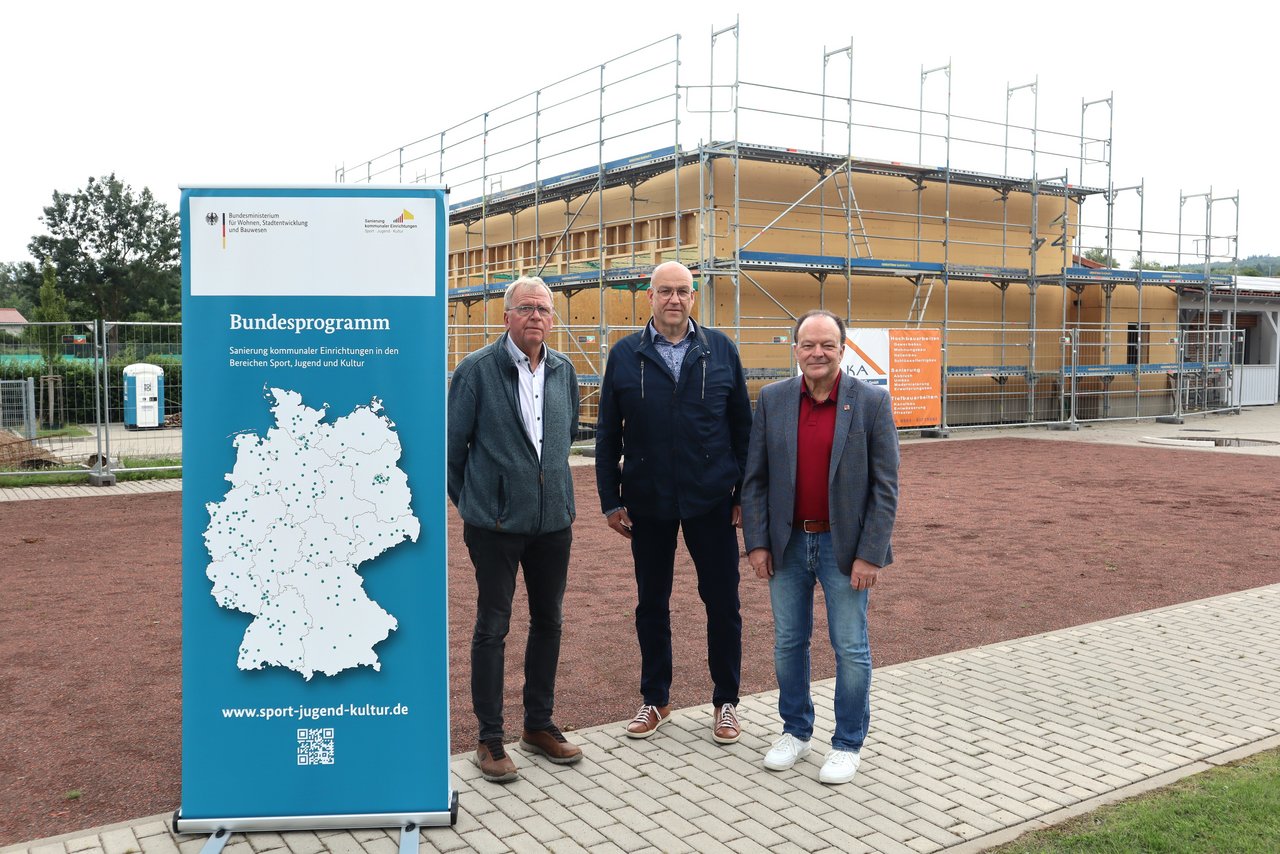 Ein Bild von drei Männern, die vor einem eingerüsteten Gebäude stehen.