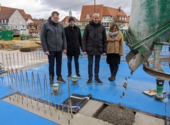 Stadt Weilheim a.d.T. Vier Personen beobachten das Einbettonieren einer Zeitkapsel