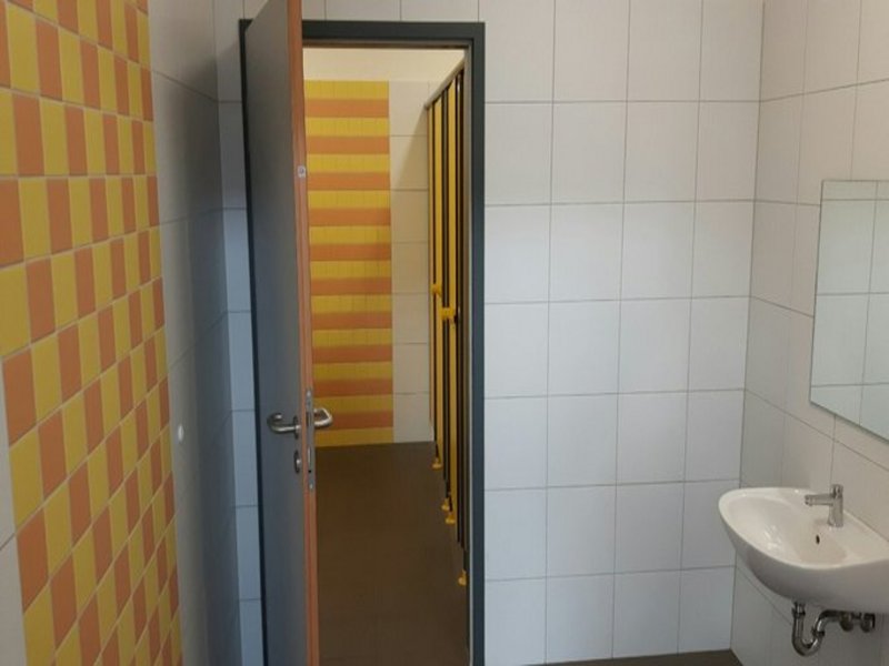 Das Bild zeigt gelb-orange geflieste Toilettenräume mit Waschbecken.