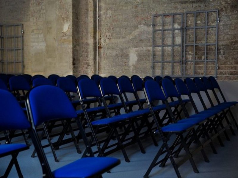Das Bild zeigt mehrere Stuhlreihen in einem Saal.
