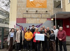 Eine Gruppe Menschen steht vor einem Gebäude und posiert für ein Foto. Zwei Personen in der Mitte halten einen Förderscheck in der Hand.