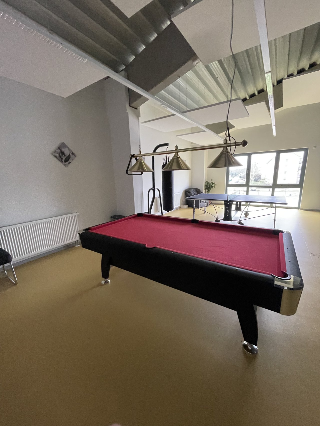 Man sieht einen Billardtisch und eine Tischtennisplatte in einem frisch sanierten Innenraum.