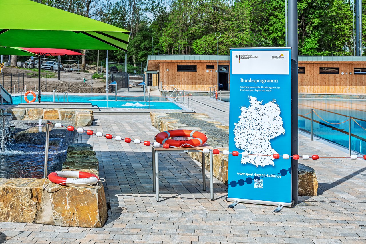 Quelle: Stadt Wuppertal/GMW Foto: Frank Buetz Ein Freibadgelände mit Roll-Up, Absperrung, Rettungsring und Sonnenschirm.
