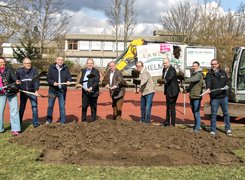 Quelle: Sebastian Dettmer Das Bild zeigt viele Menschen, die aufgereiht vor einem Sportplatz stehen und einen Spaten in der Hand haben. Lachend graben sie symbolisch etwas Erde aus.