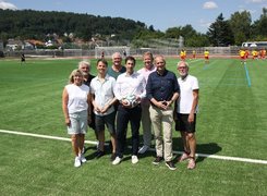 Quelle: Stadt Hann. Münden Das Bild zeigt acht Personen bei der Einweihung einer Sportanlage. Im Hintergrund wird Fußball gespielt.