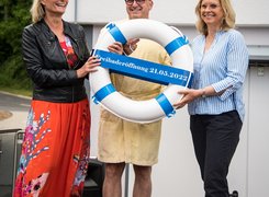 Das Bild zeigt drei Personen, die einen symbolischen Rettungsring halten.
