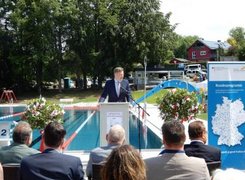 Markt Zell im Fichtelgebirge Das Bild zeigt einen Mann, der vor einem Publikum eine Rede hält. Im Hintergrund ist das Schwimmerbecken eines Freibades zu sehen.