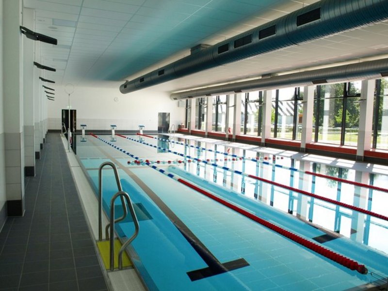 Das Bild zeigt ein Schwimmbecken in einem Hallenbad, seitlich ist eine Fensterfront zu sehen.