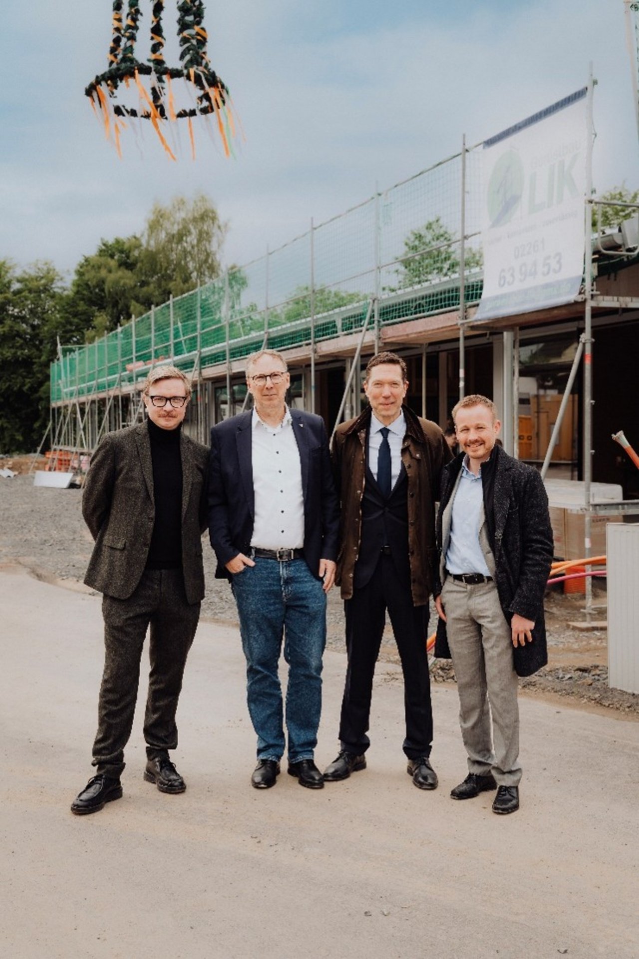 Quelle: OTTO QUAST Bau Aktiengesellschaft Das Bild zeigt vier Männer vor der Baustelle der Sporthalle.