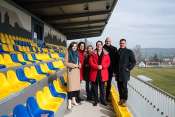 Copyright: Stefanie Loos Eine Gruppe Menschen stehe auf einer Tribüne eines Stadions.