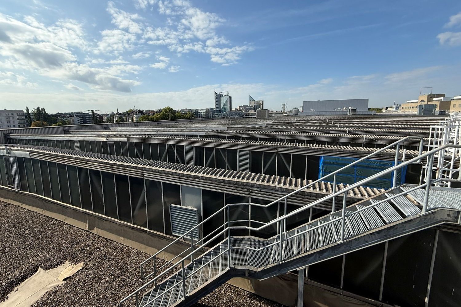 o MMaximilian Gens / Düsseldorfer Schauspielhaus Das Bild zeigt das Dach des Schauspielhauses mit Metallgeländer und Treppe, im Hintergrund Stadtgebäude.
