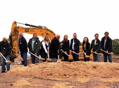 Das Bild zeigt Personen, die einen Spatenstich durchführen. Im Hintergrund ist ein Bagger zu sehen.