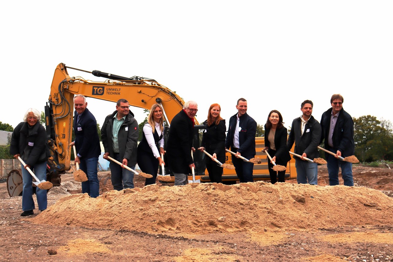 Das Bild zeigt einen Spatenstich mit Bagger im Hintergrund.