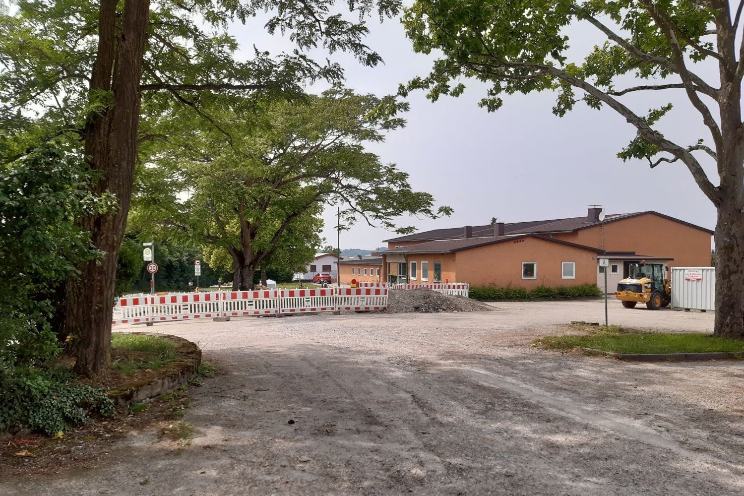 Stadt Bad Friedrichshall Da Bild zeigt ein eingeschossiges Gebäude mit oranger Fassade und einen Bagger neben Erdhügeln und einer rot-weißen Absperrung.