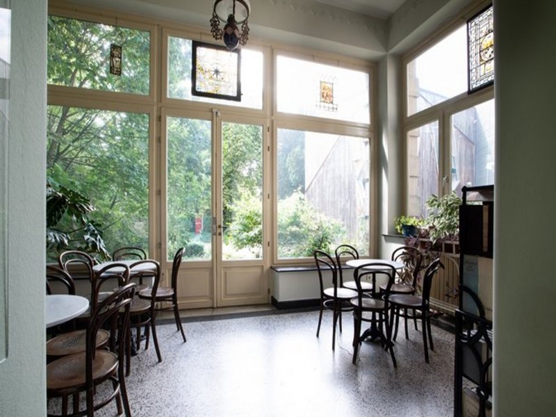 Das Bild zeigt einen leeren Gastraum mit Fensterfront, Tischen und Stühlen.