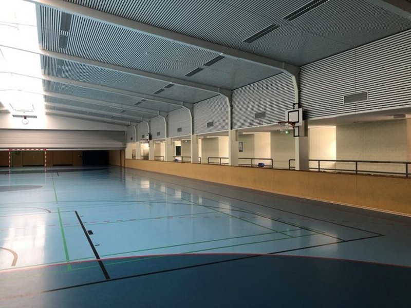 Das Bild zeigt eine Sporthalle mit blauem Boden, bunten Linien und Basketballkorb.