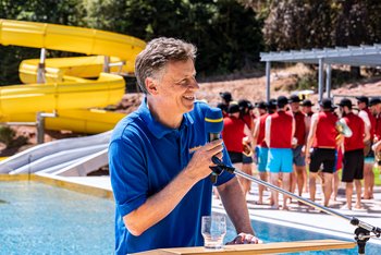 Quelle: Stadtwerke Schramberg Eigenbetrieb e.K. Das Bild zeigt einen Mann in einem Freibad, der in ein Mikrofon spricht.